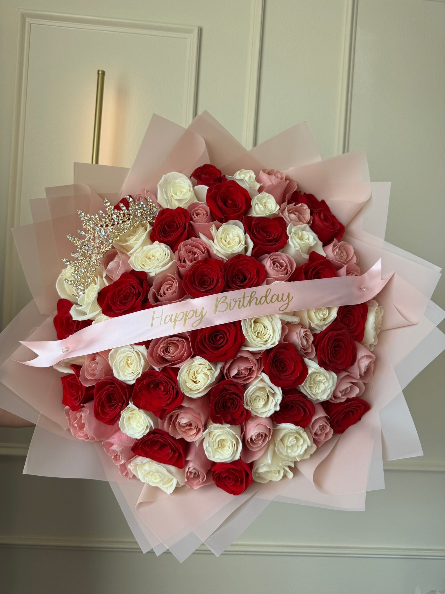 Bouquet of red, white, and pink roses with a 'Happy Birthday' ribbon on a neutral background.